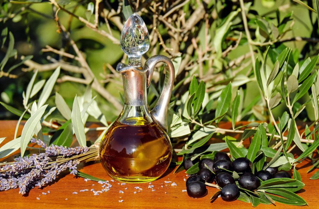 Glass cruet filled with extra virgin olive oil surrounded by black olives and olive branches